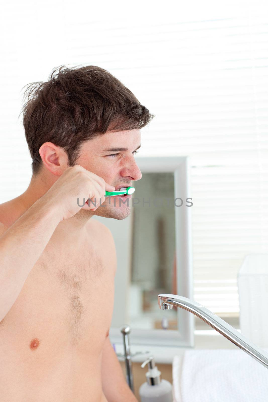 Good-looking young man brushing his teeth in the bathroom at home