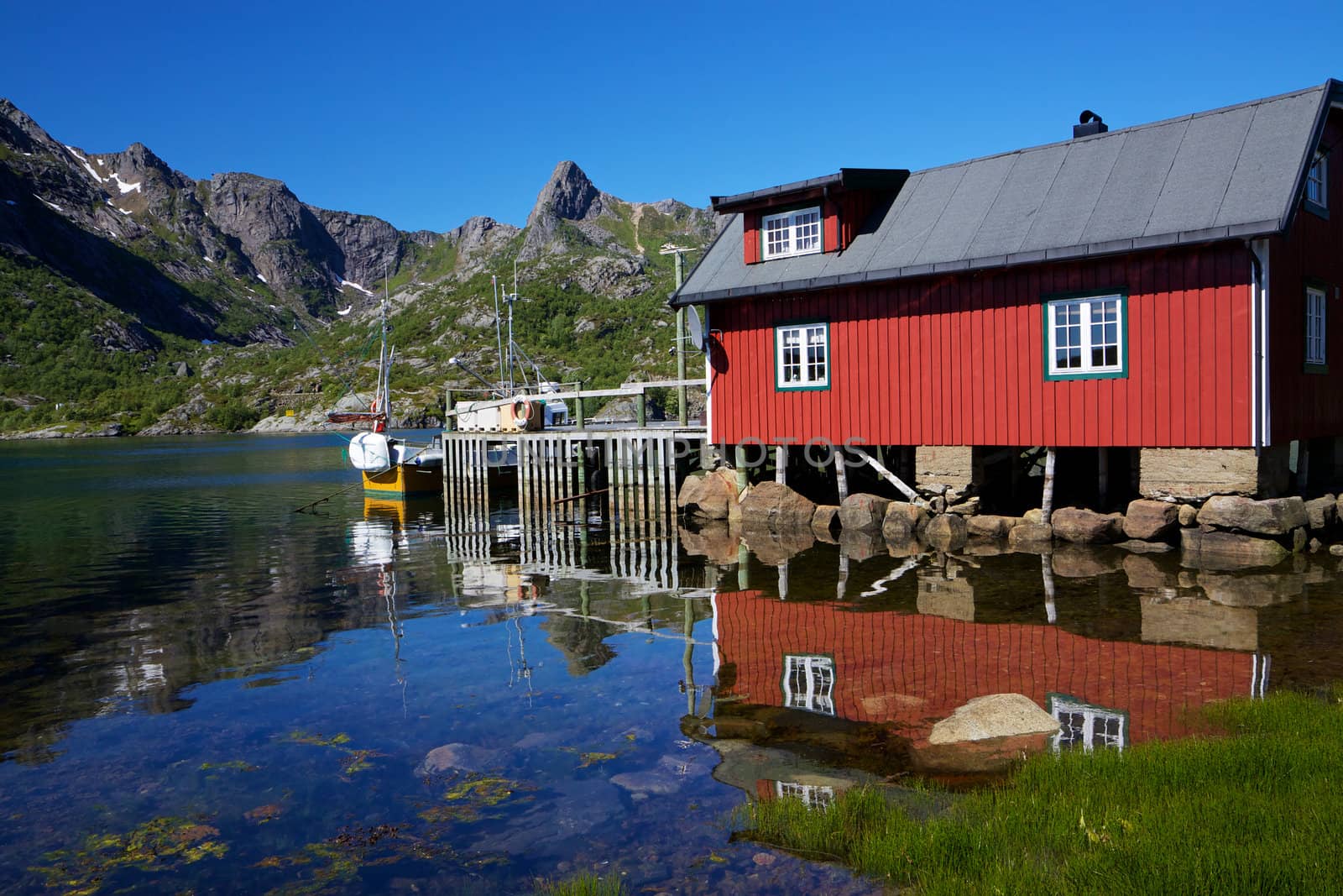Typical red modern fishing hut on Lofoten islands in Norway reflecting in fjord