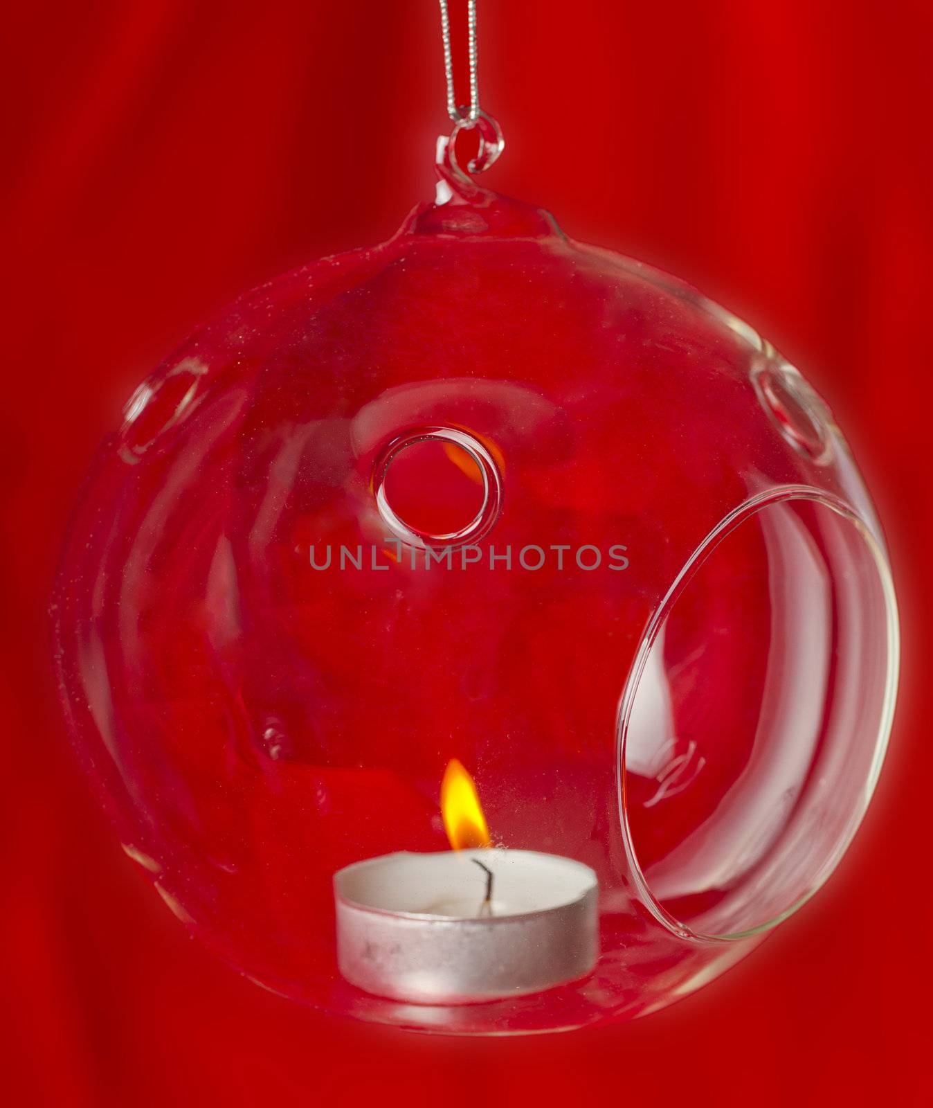 Glass bauble with lite candle over red background