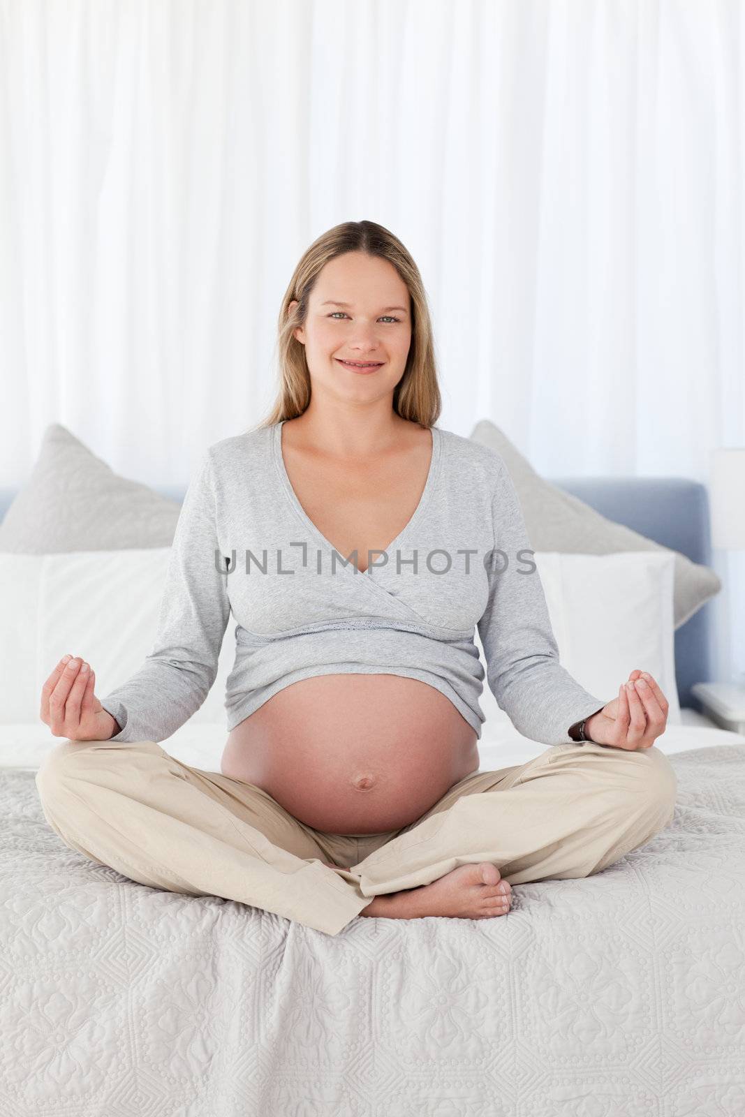 Pretty pregnant woman doing yoga on a bed
