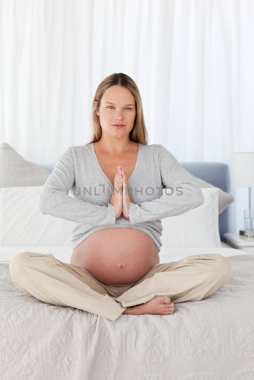 Serious pregnant woman doing yoga sitting on the bed