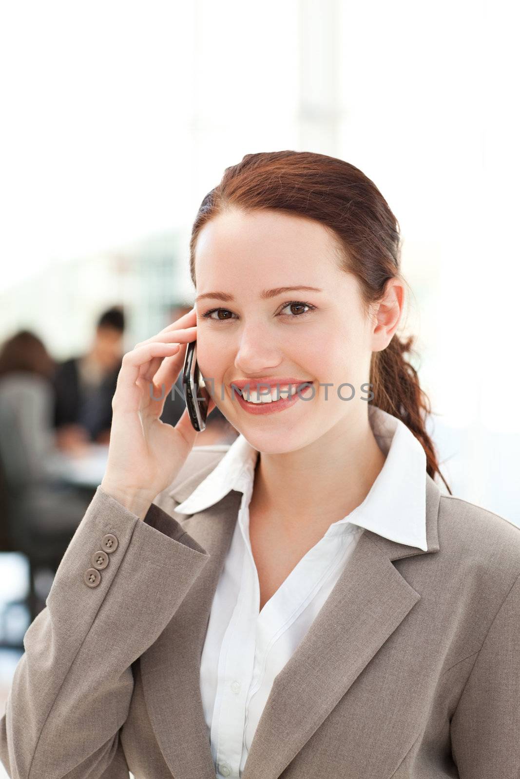Cute businesswoman on the phone in the foreground while her team is working in the office