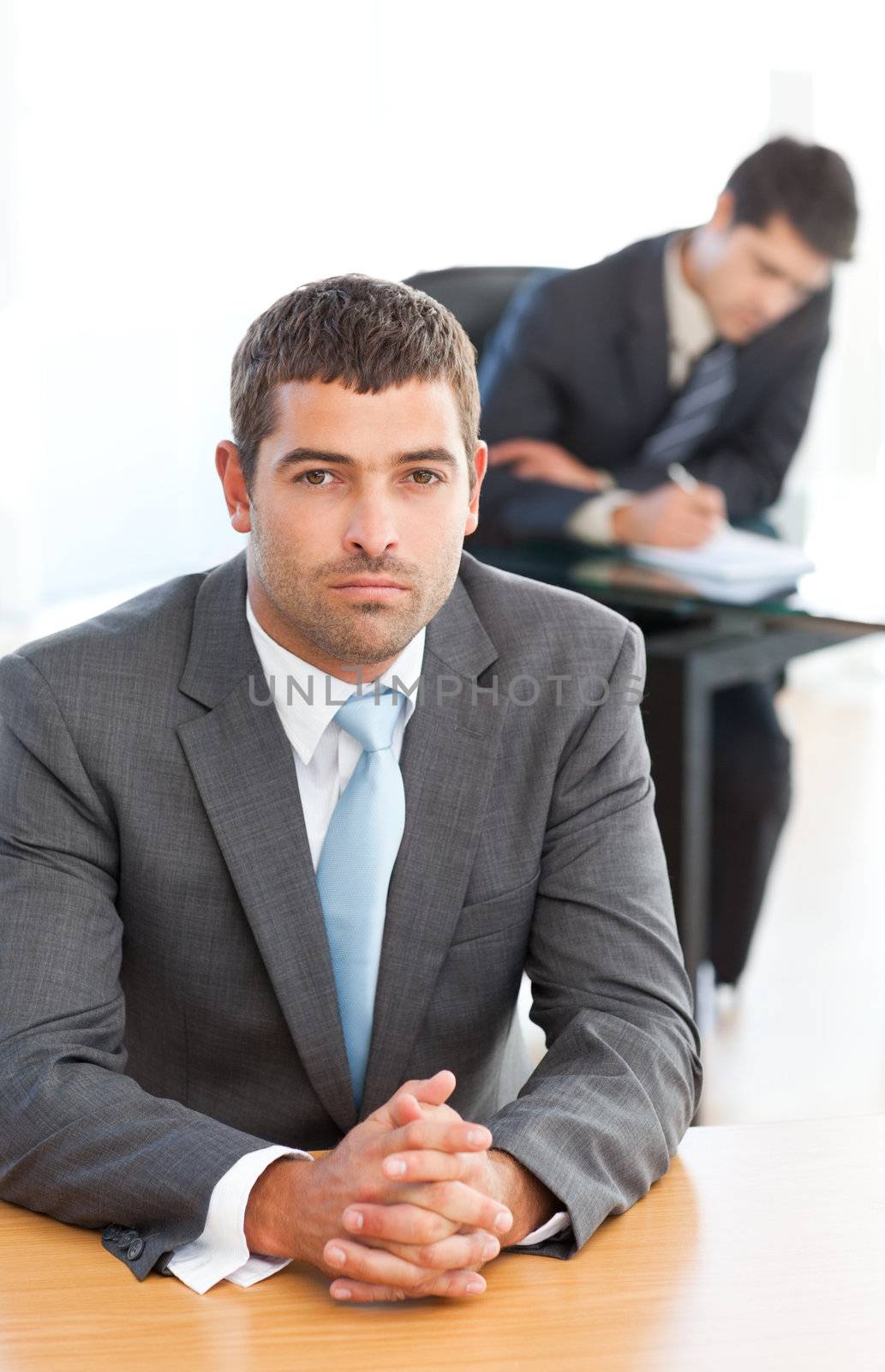 Charismatic businessman sitting in the foreground while his colleague is working at a table