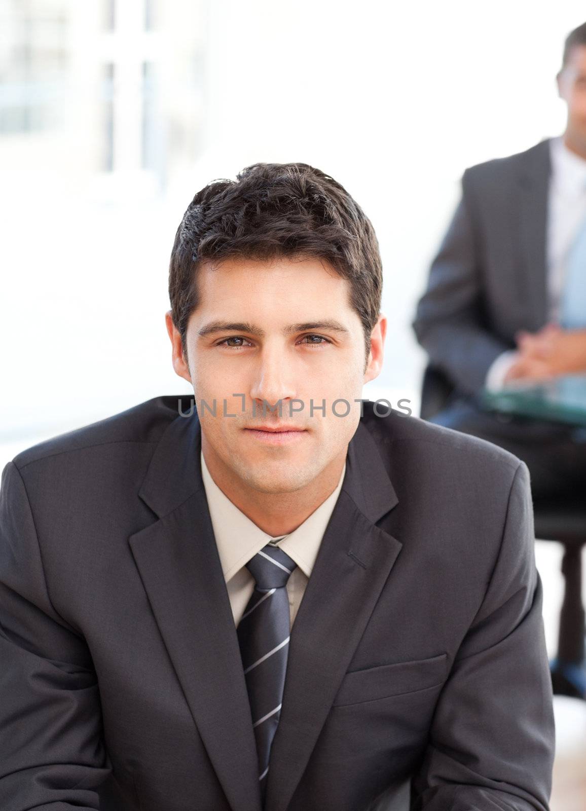 Serious businessman during an interview with a co-worker waiting in the background