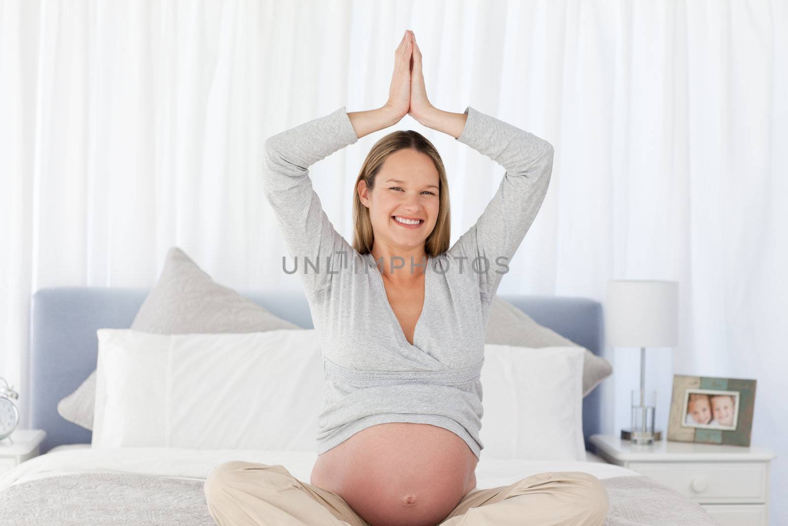 Smiling pregnant woman doing yoga on the bed at home