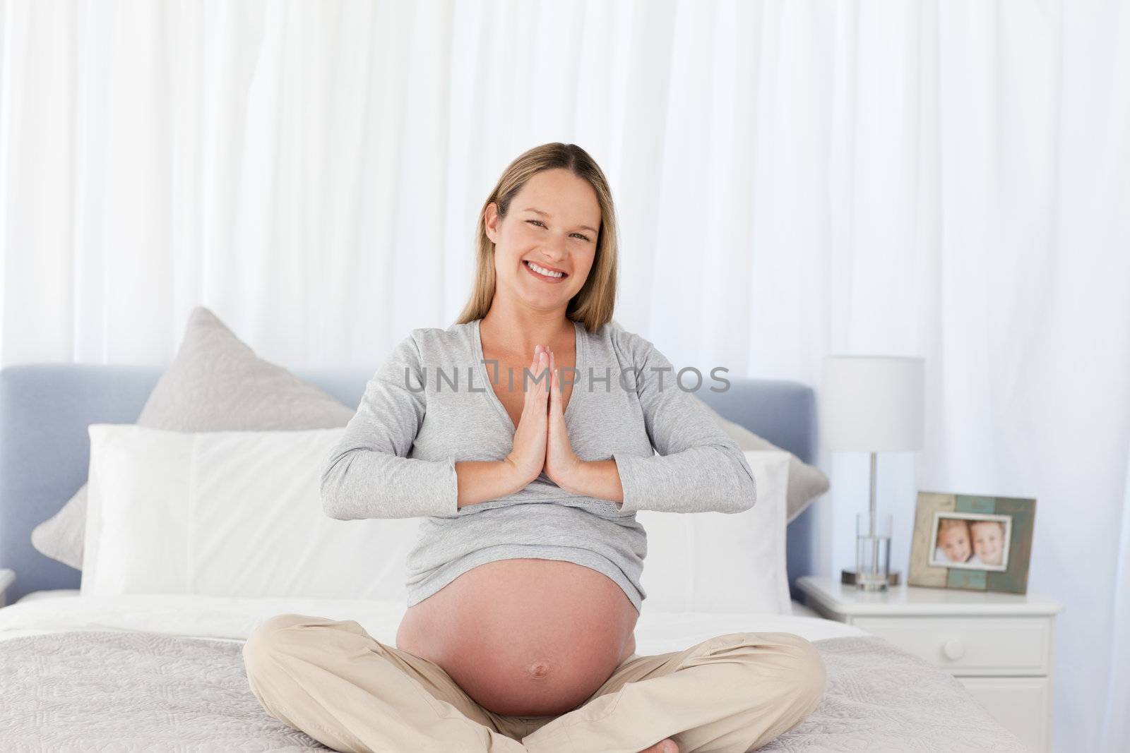 Adorable future mom doing meditation sitting on the bed at home