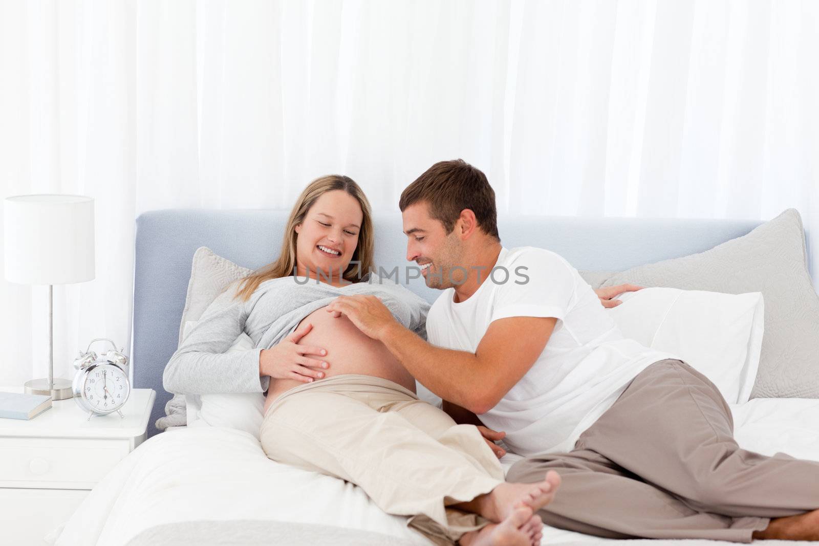 Cute man playing with his pregnant wife while relaxing on the bedroom