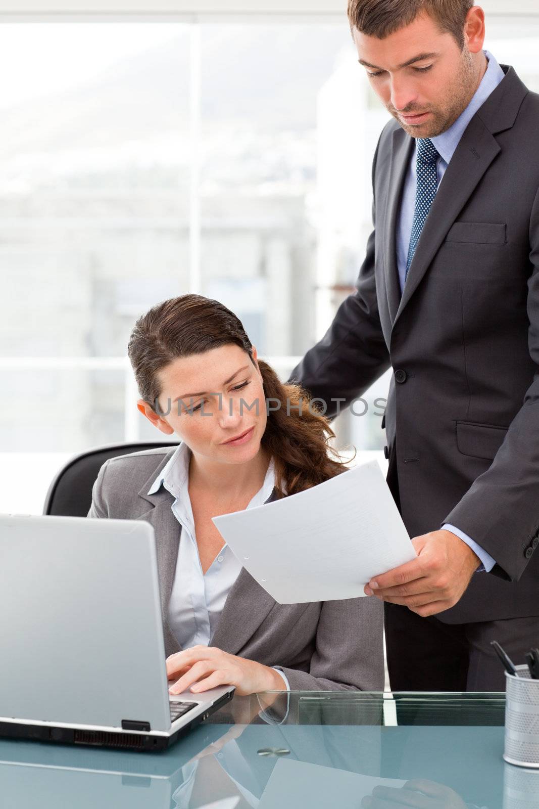 Handsome manager showing a paper to a businesswoman while working on the laptop in the office