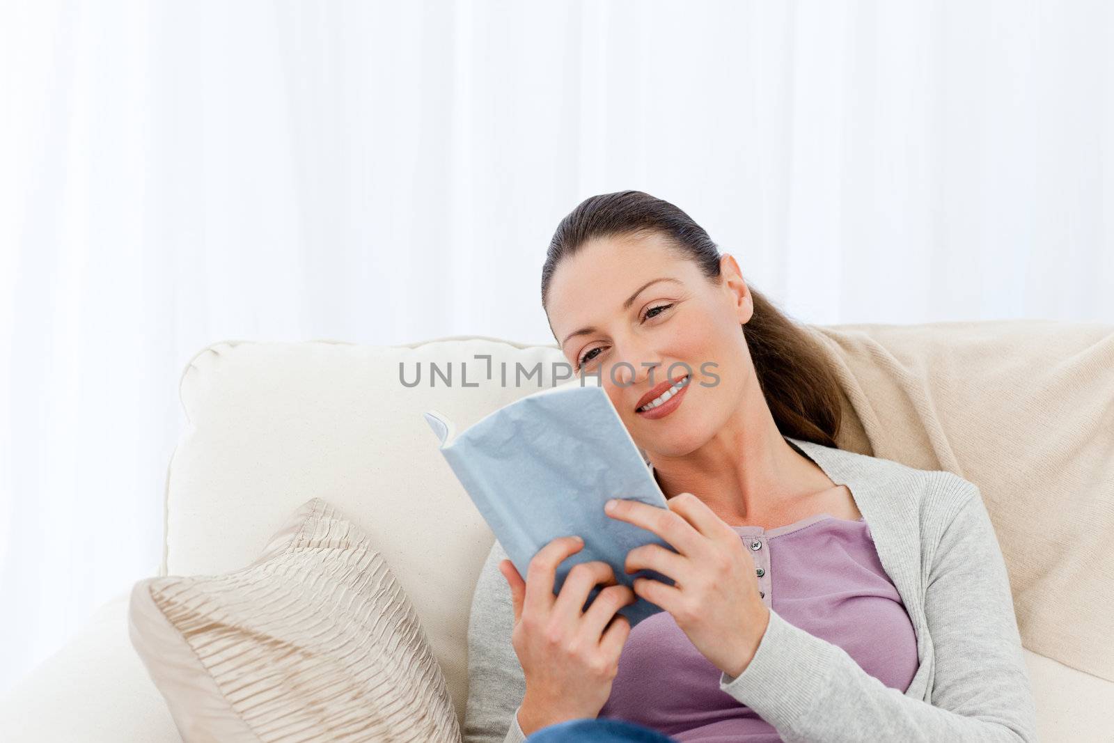 Lovely woman reading a romance sitting on the sofa at home