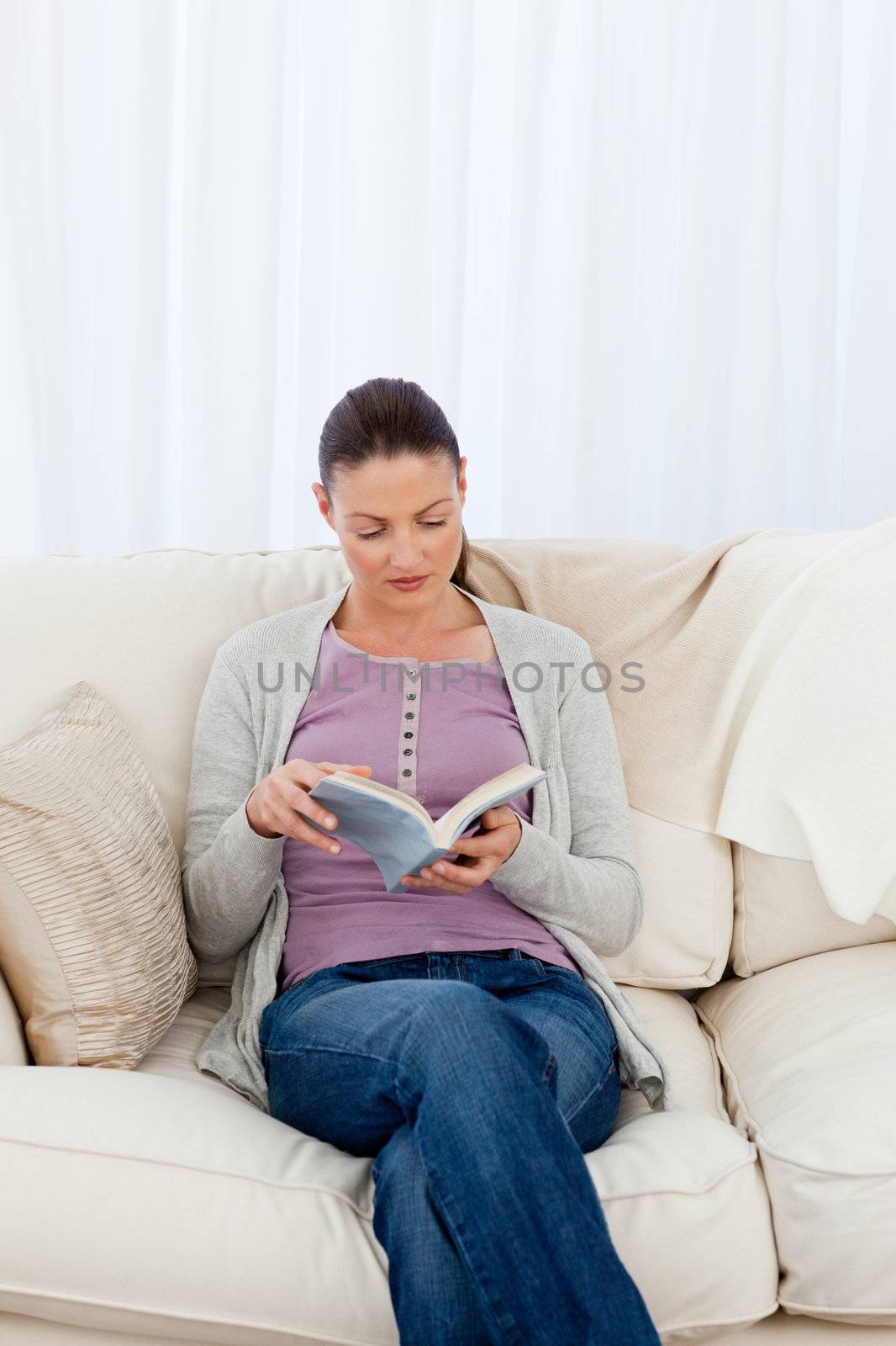 Attentive woman reading a book on the sofa of her living room