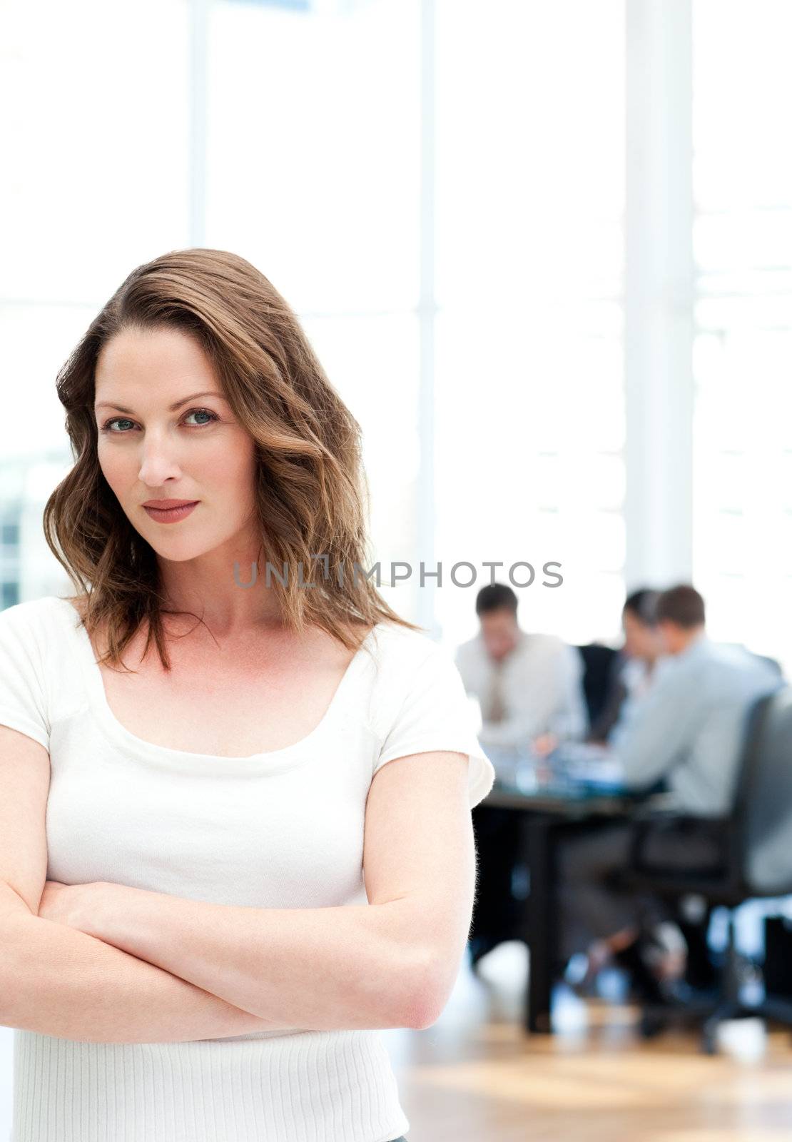 Confident woman standing at a meeting while her team working in the background