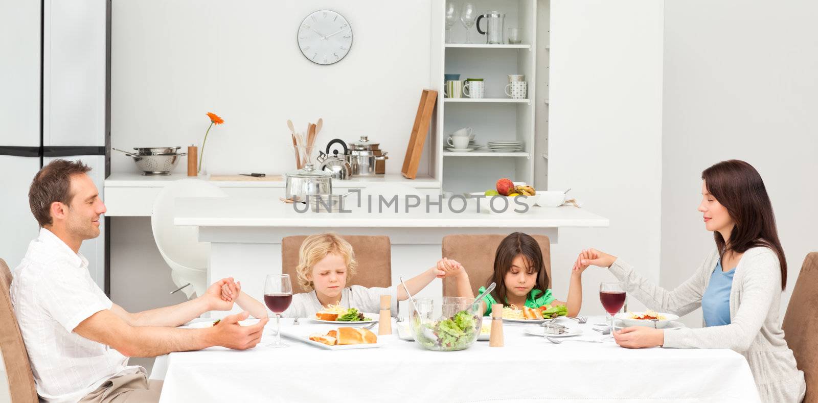 Concentrated family praying before having lunch  by Wavebreakmedia
