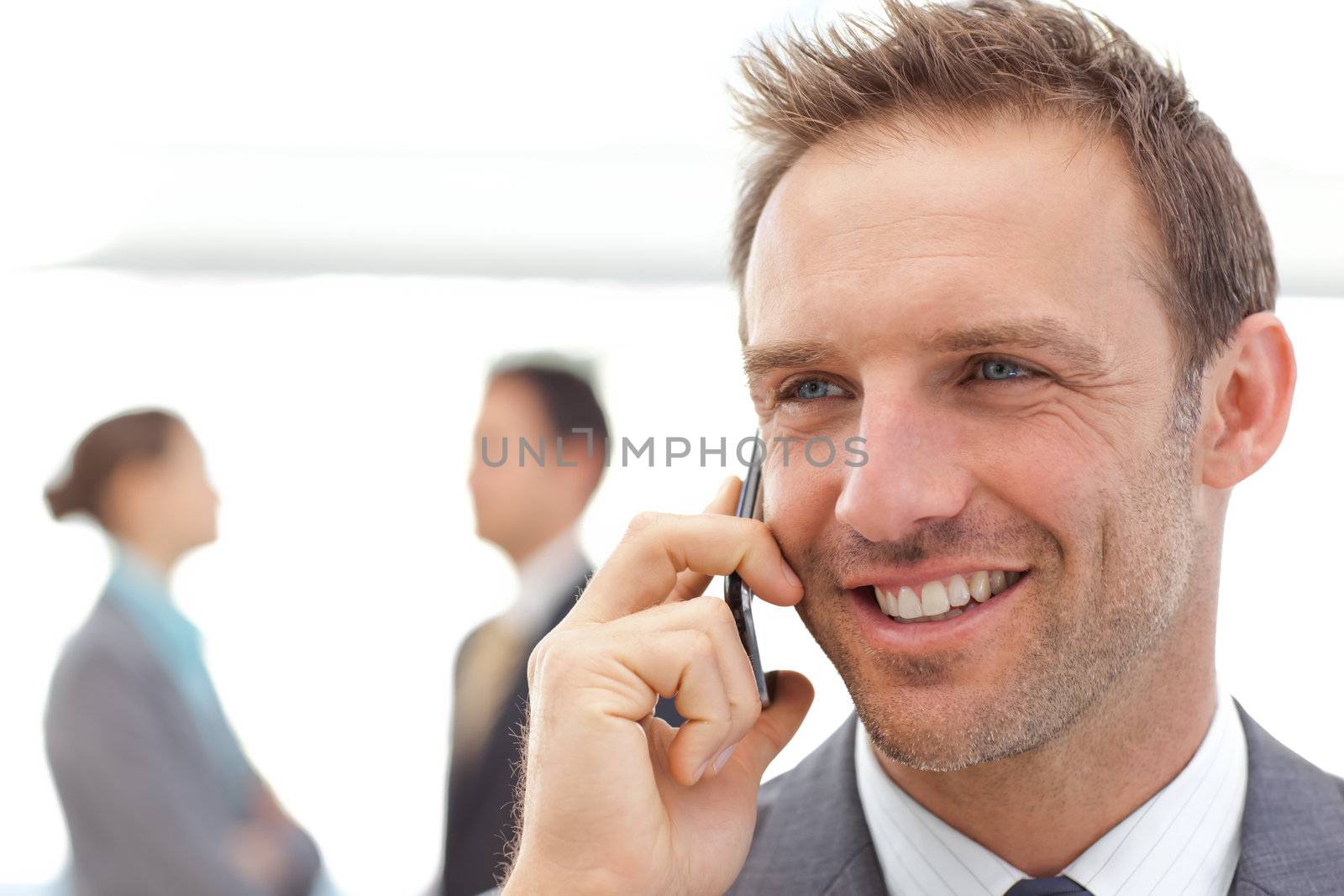 Handsome businessman on the phone while his partners standing on the background