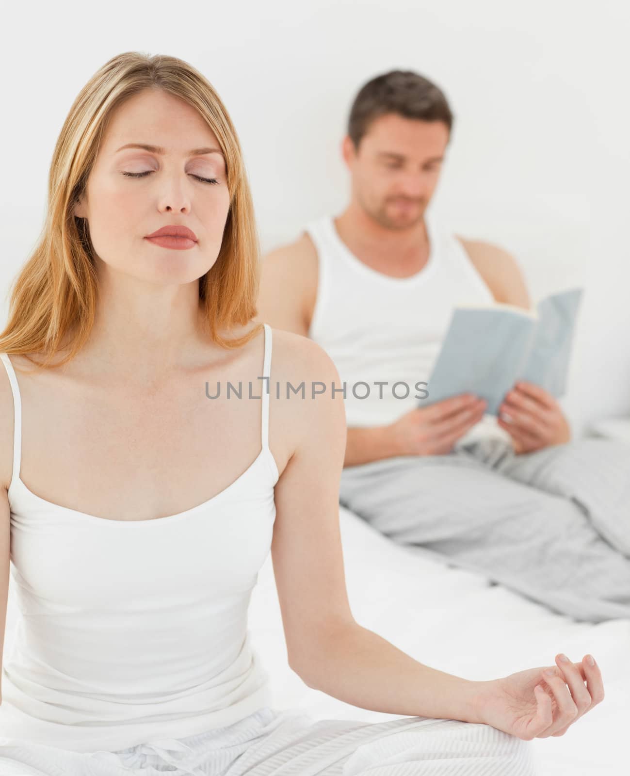 Woman practicing yoga while her husband is reading on the bed