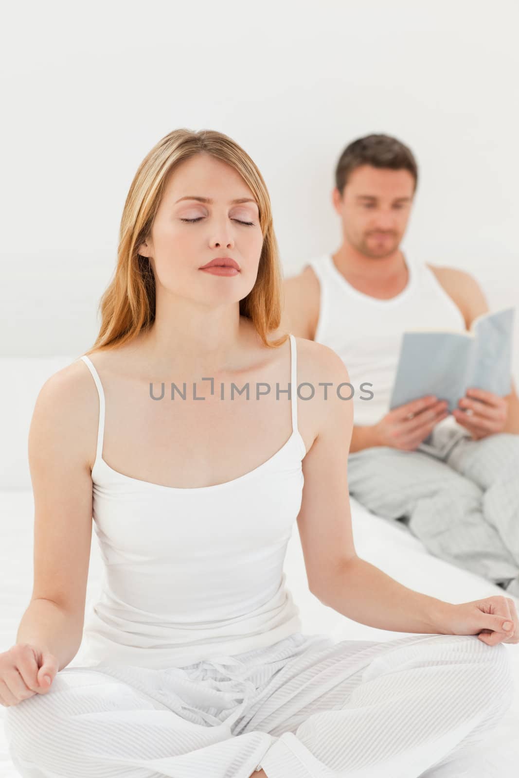 Woman practicing yoga while her husband is reading on the bed