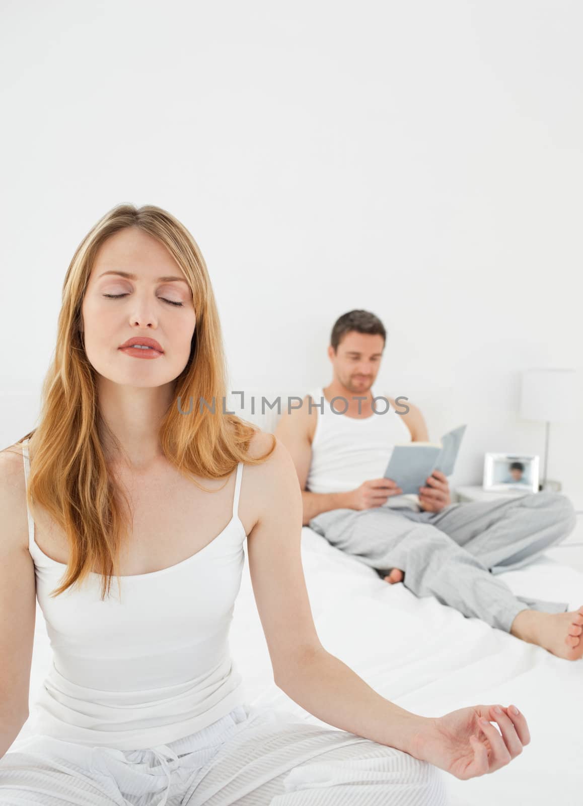 Woman practicing yoga while her husband is reading on the bed