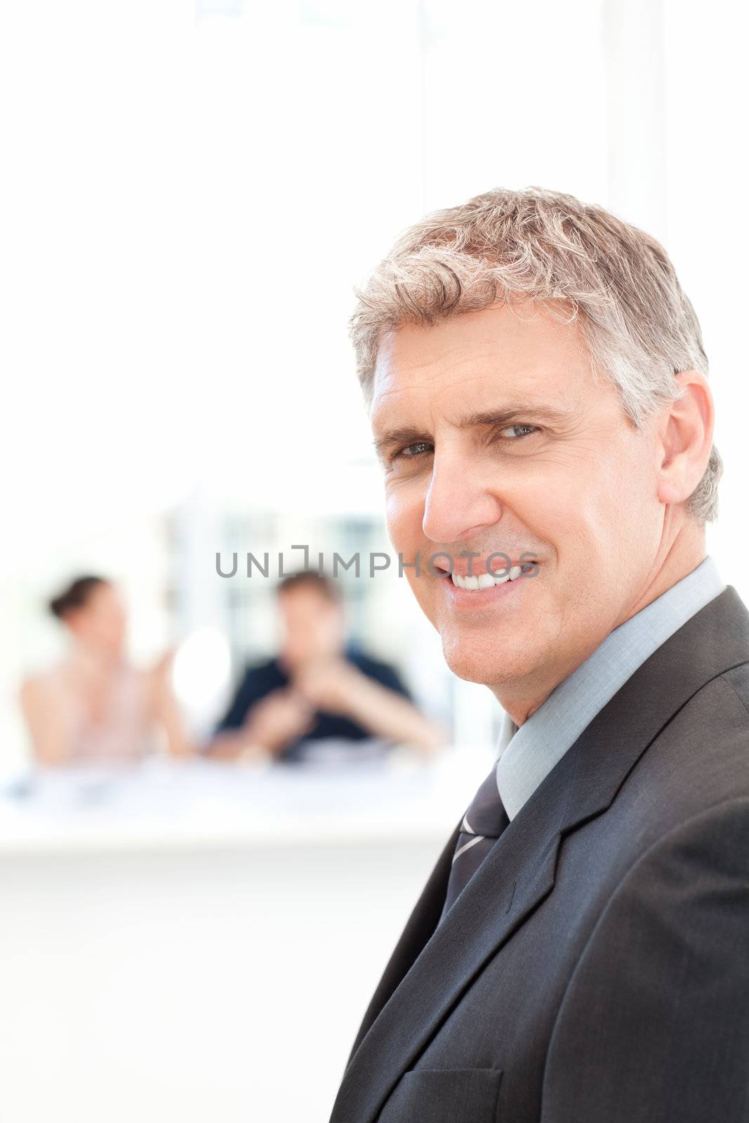 Businessman looking at the camera while his team is working in the background
