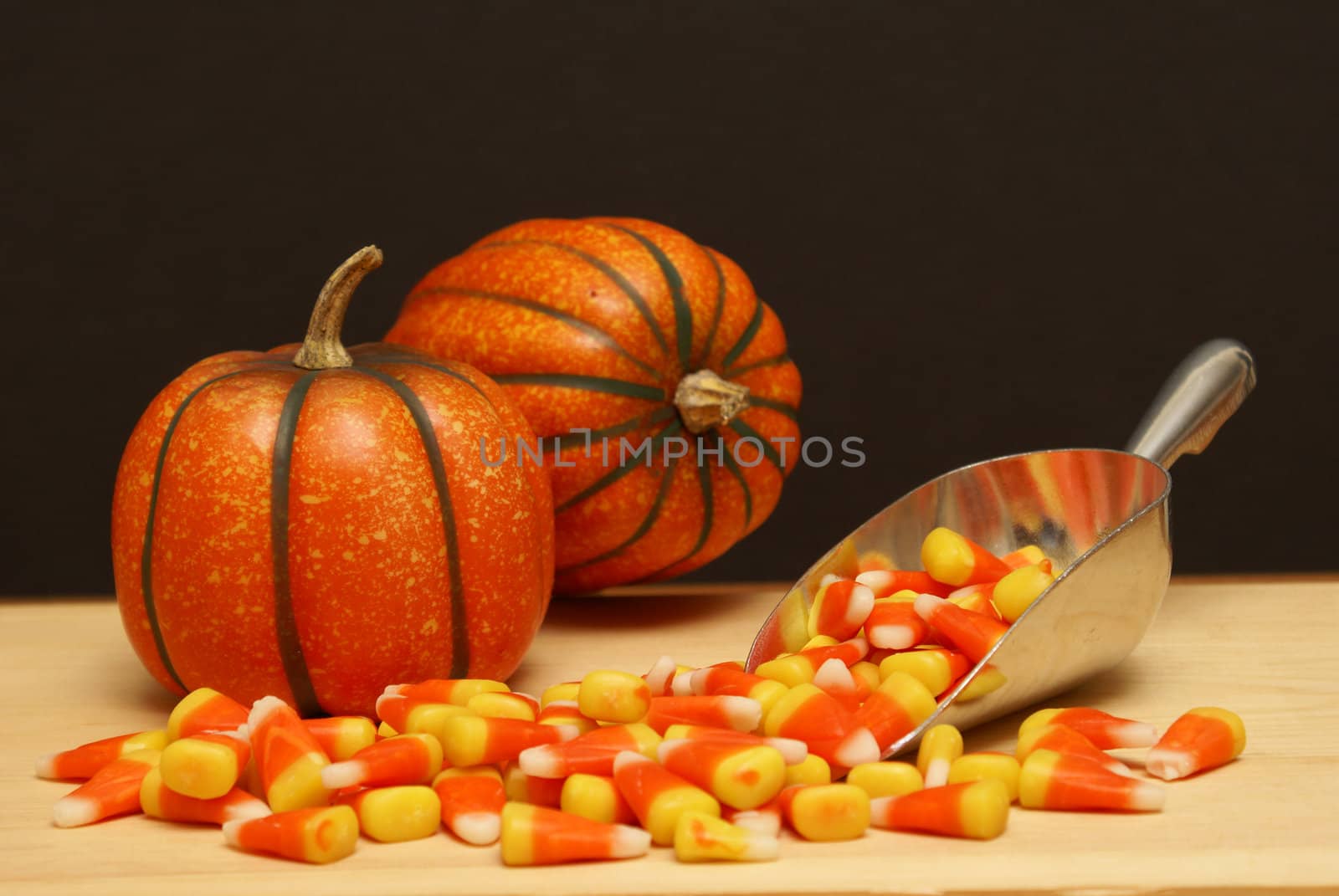 A scoop of candy corn next to pumpkins.