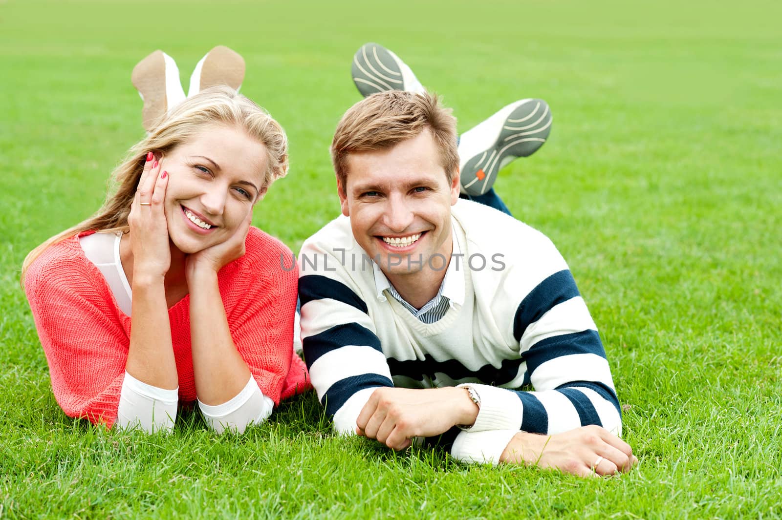 Happy young couple outdoors. Lying on lush green grass