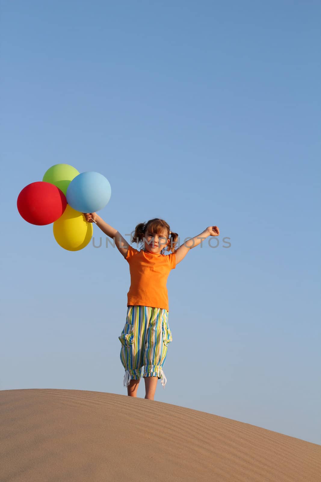 happy little girl with balloons standing on sand dune
