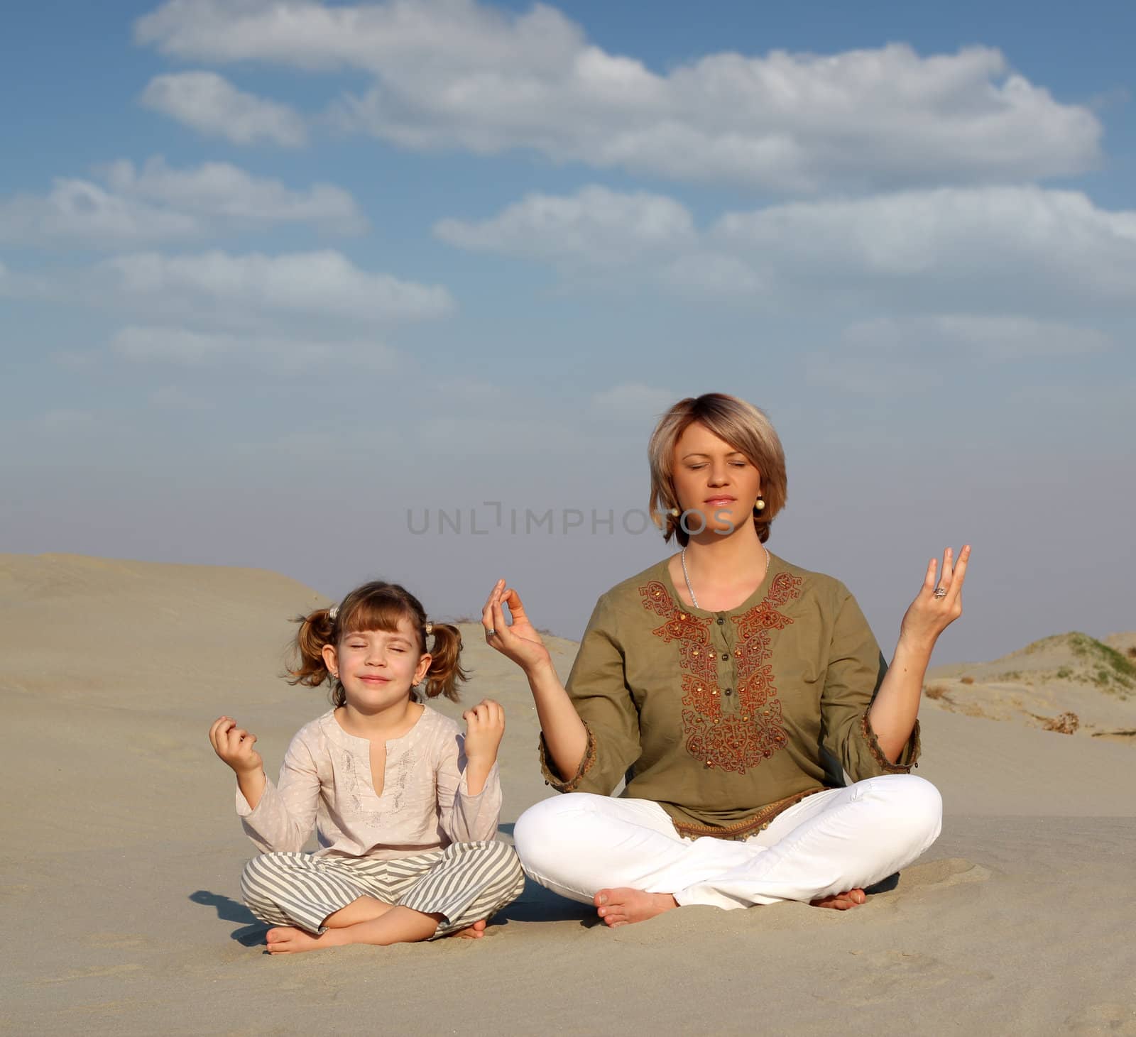 mother and daughter meditating in desert by goce