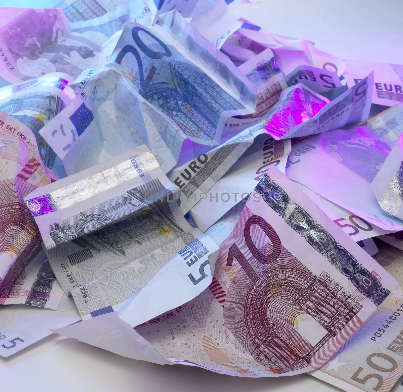 studio photography of crumbled euro banknotes illuminated with colored light