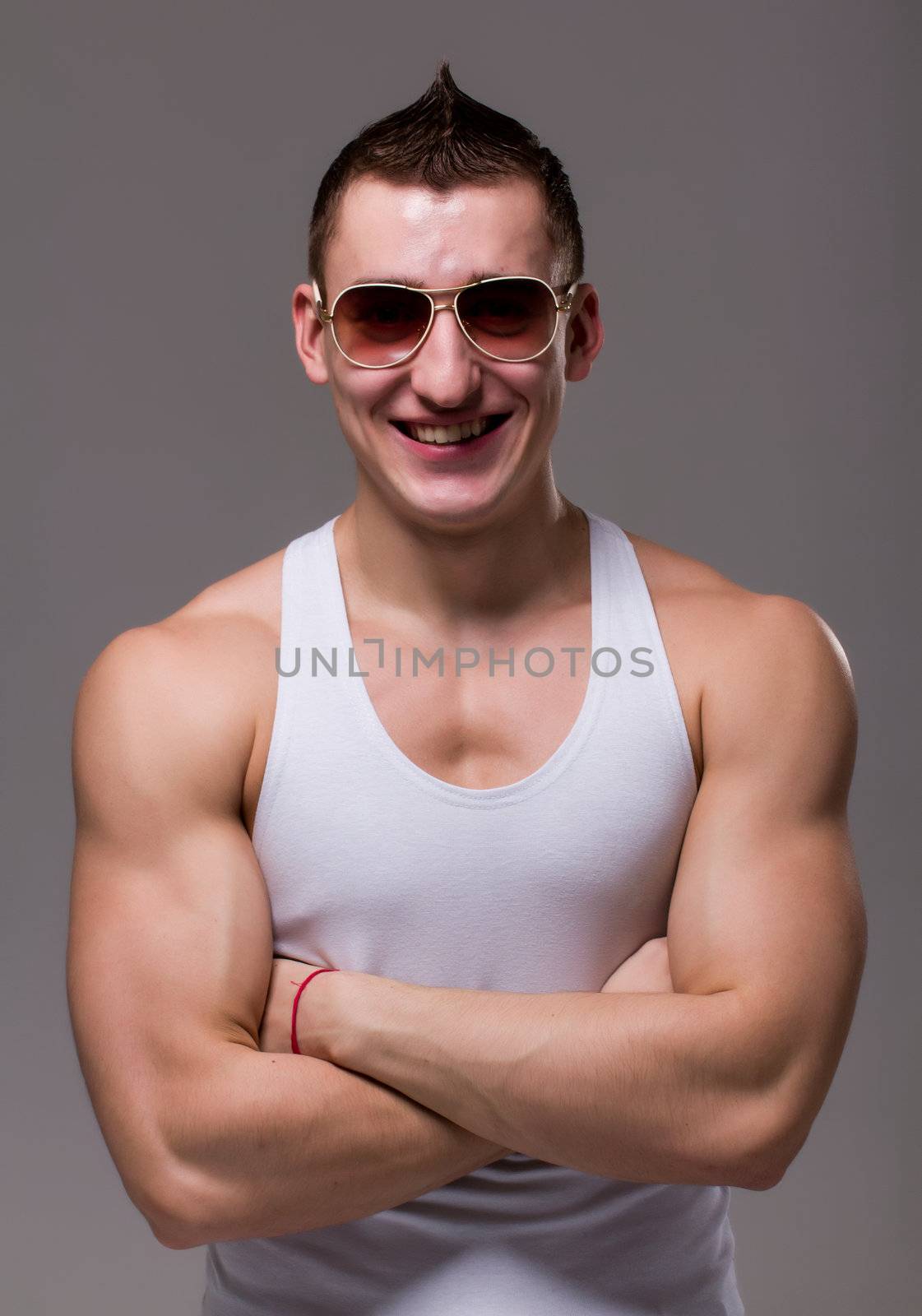 Muscular man wearing black sunglasses posing on a gray background