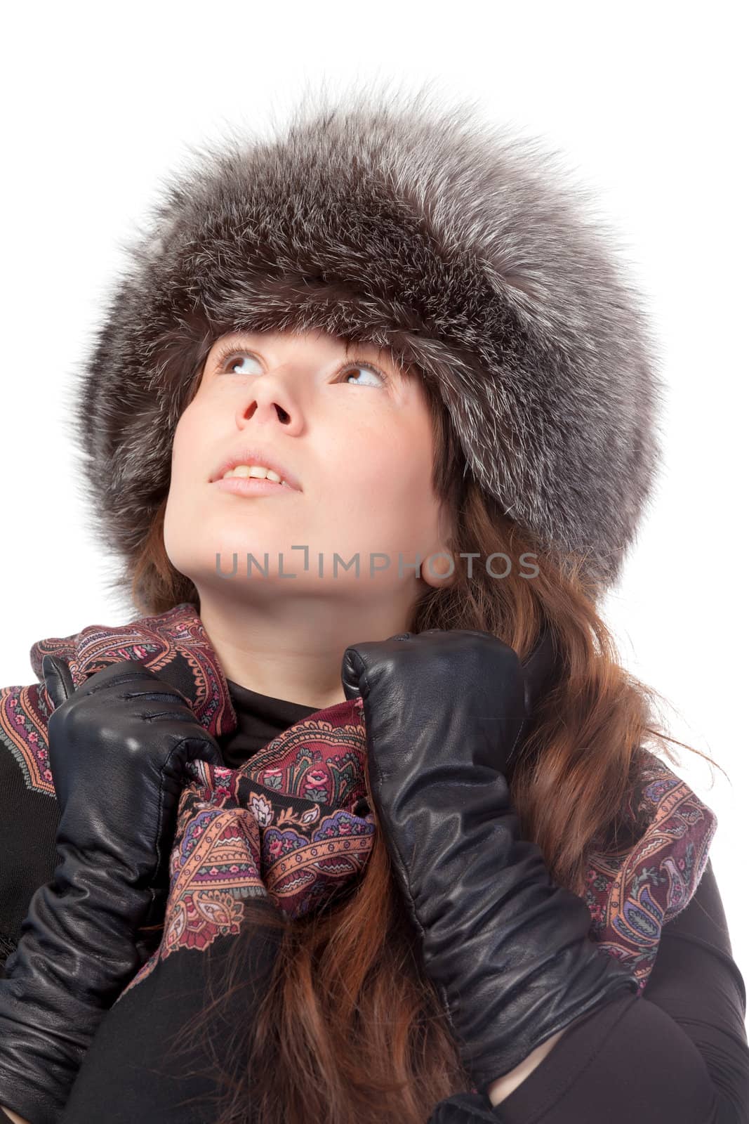 Elegant fashionable woman in winter outfit wearing a scarf, leather gloves and warm fur hat looking up into the sky deep in thought