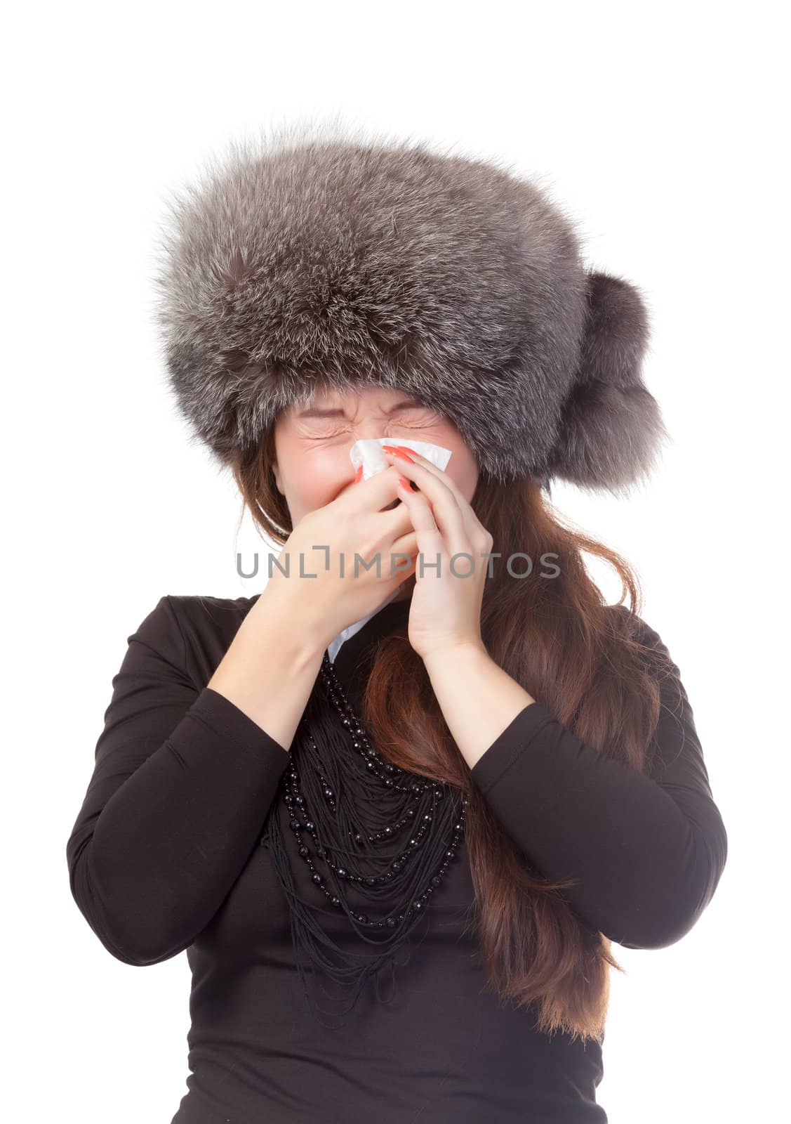 Woman with a winter cold and flu wearing a warm fur hat and blowing her nose on a tissue isolated on white