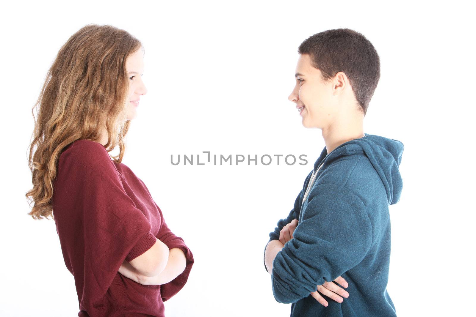 Young teenaged couple standing facing each other in profile to the camera smiling at each other with their arms folded isolated on white