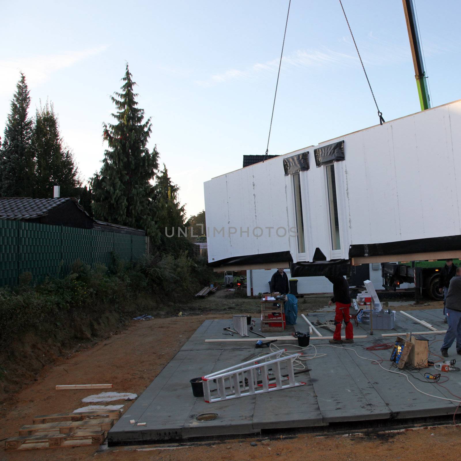 Crane delivering an external wall section of a prefabricated timber house which is hanging suspended midair over the foundations Crane delivering an external wall section of a prefabricate timber house which is hanging suspended midair over the foundations