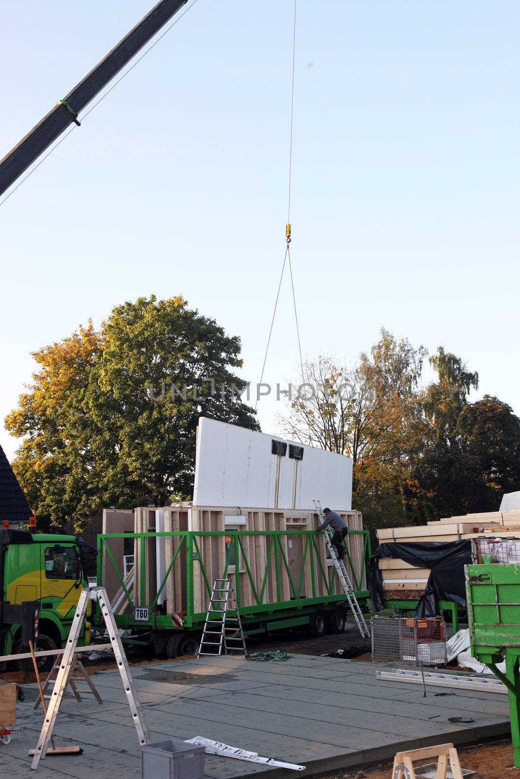 Crane lifting a section of a prefabricated timber house out of the housing on the specially adapted trailer used to transport it to the building site