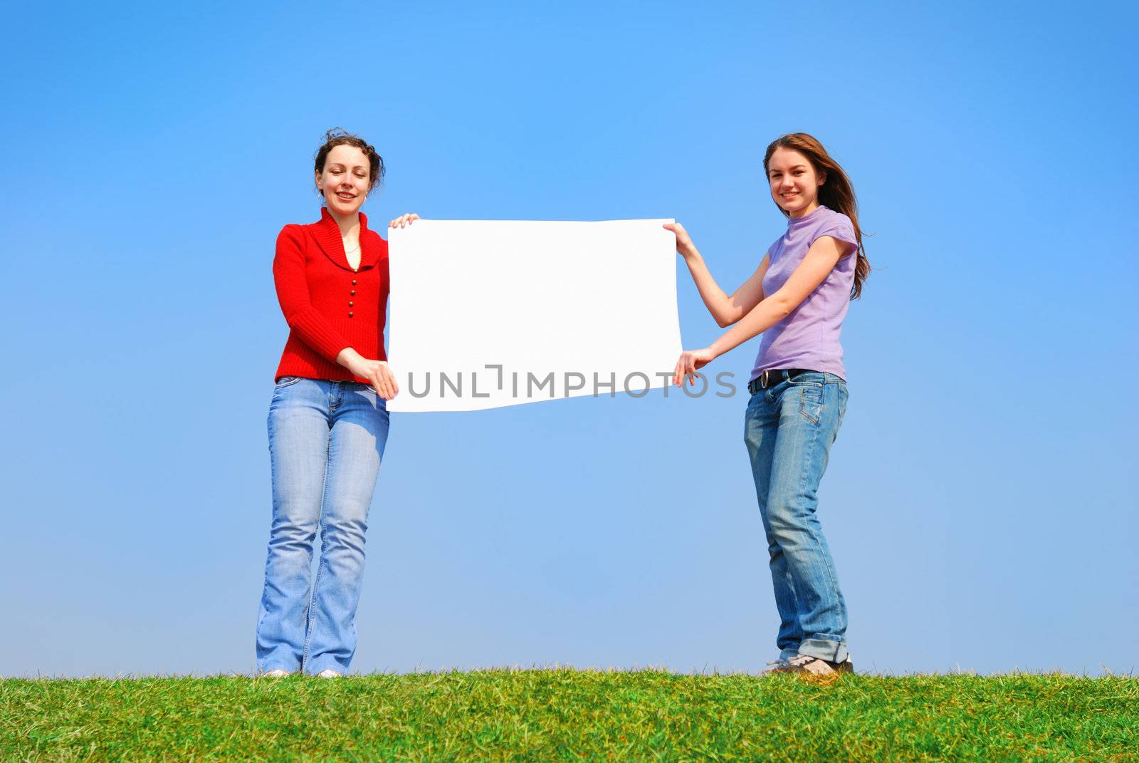 Girls holding blank sheet against blue sky