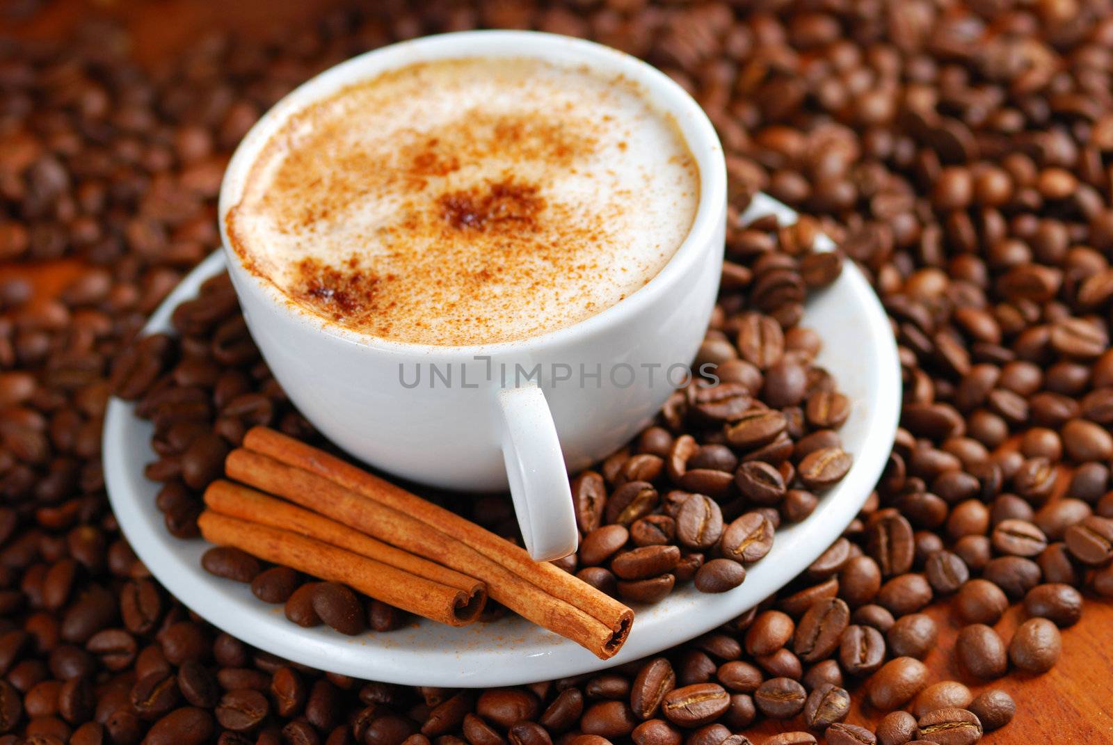 Cup of cappuccino  with cinnamon and spilled out coffee beans.