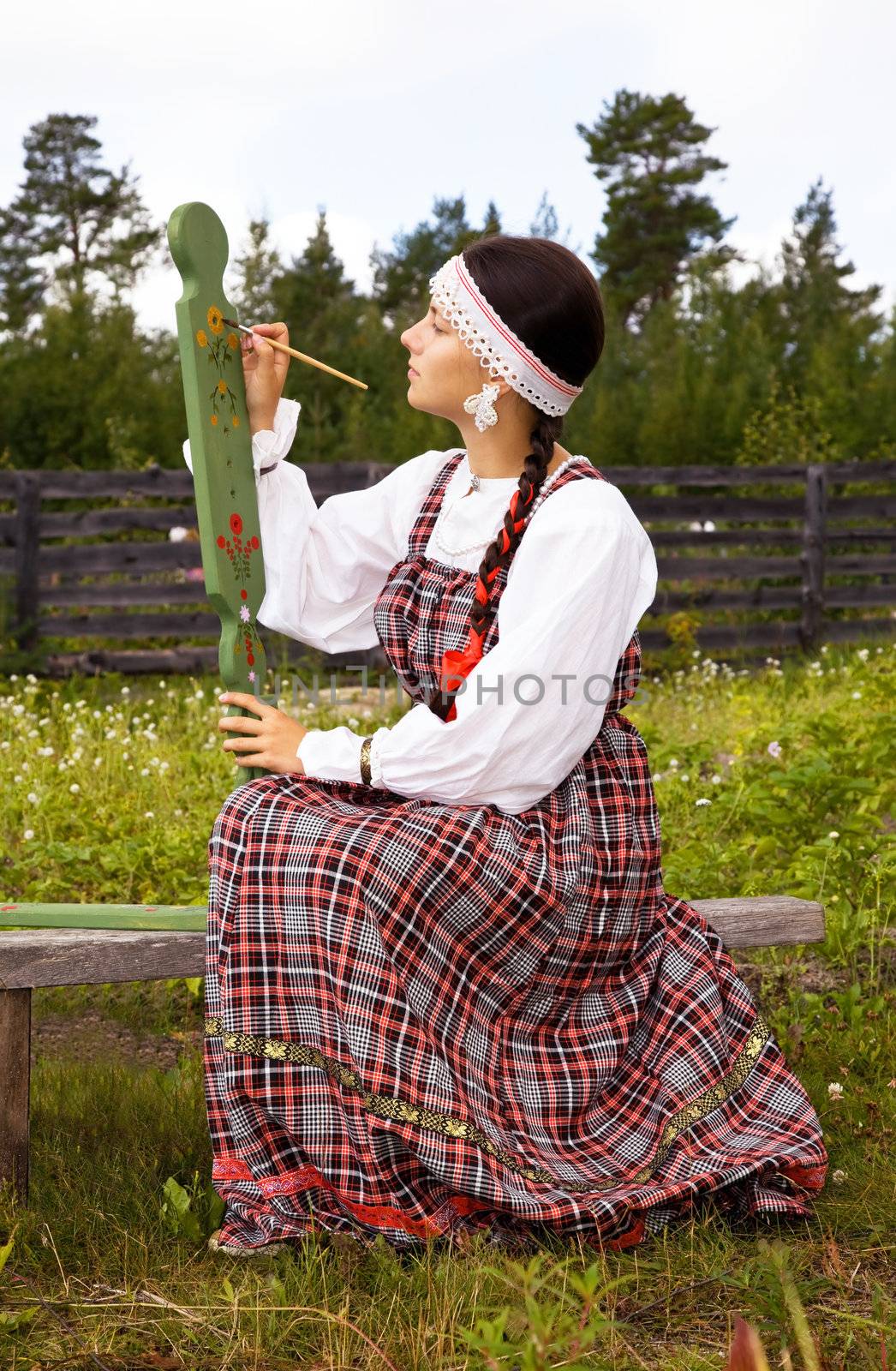 Girl in national costume paints a spinning wheel .Summer. Country Landscape