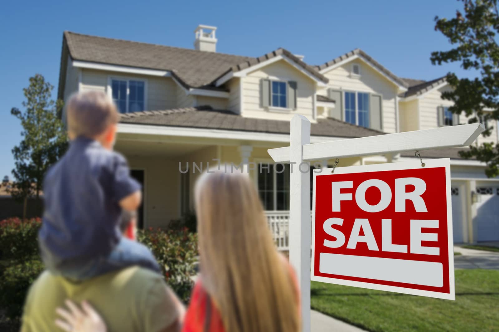 Young Family Looking at a Beautiful New Home with a For Sale Real Estate Sign in Front.