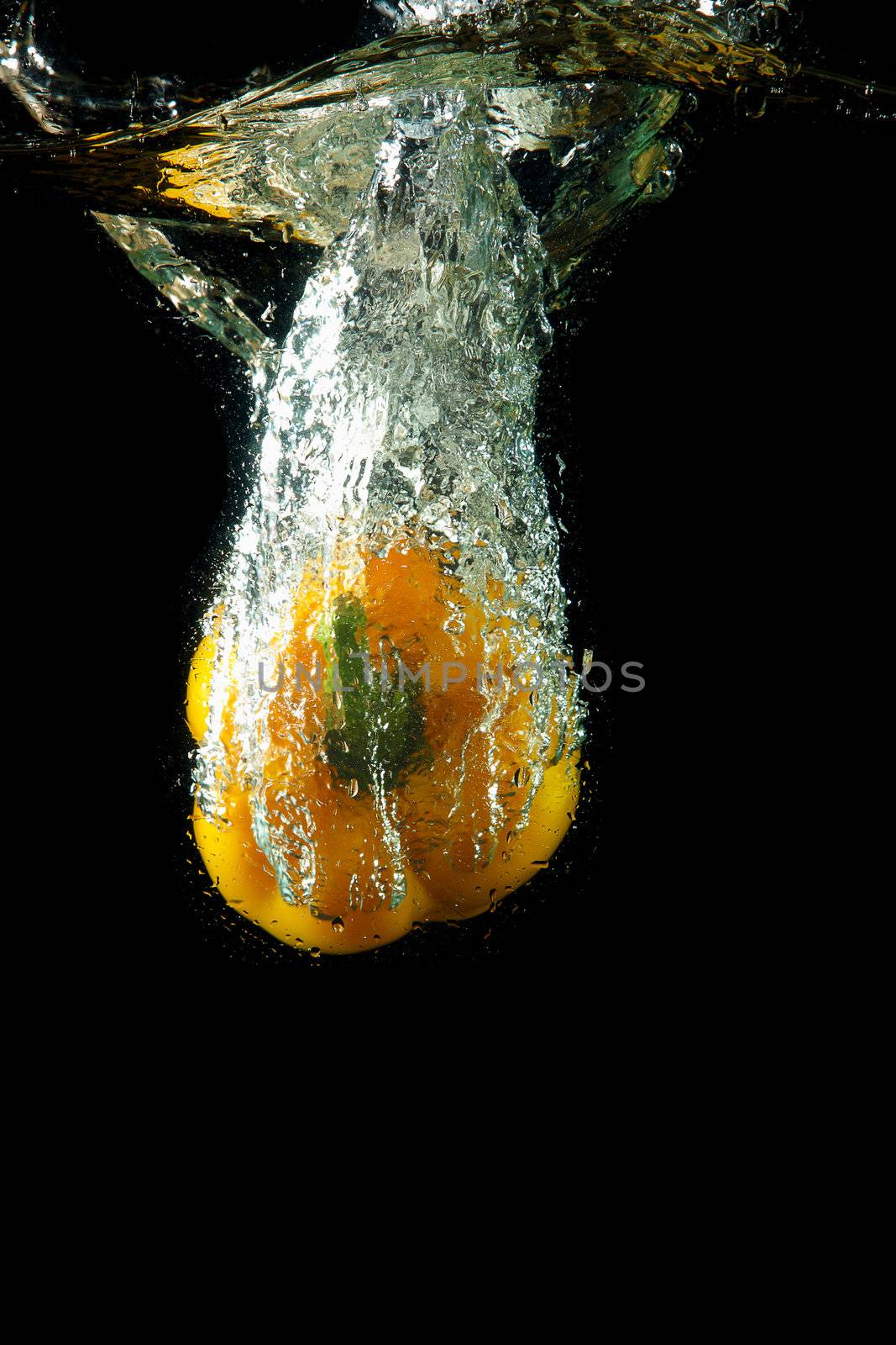 Colored yellow paprika in water splashes on black background