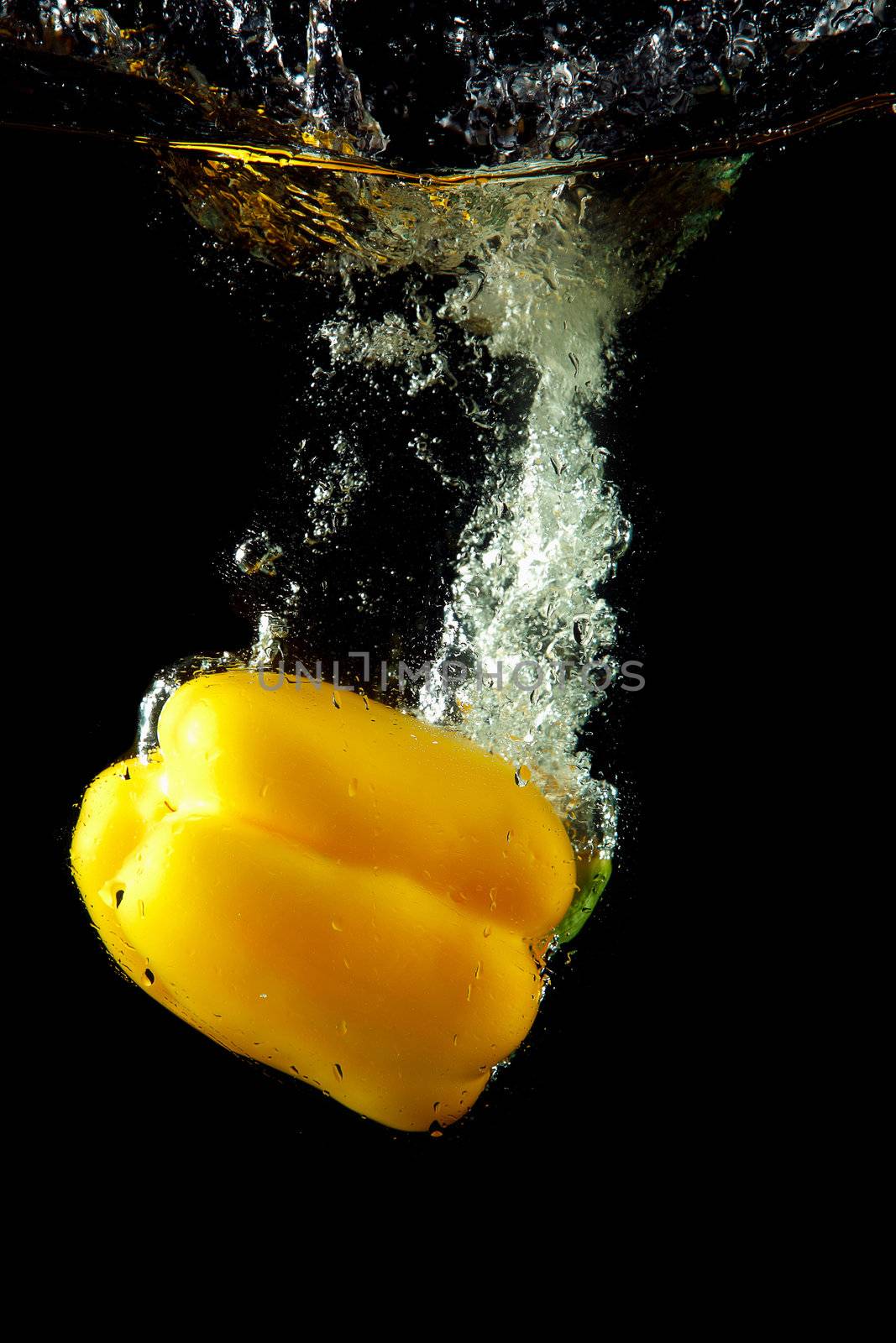 Colored yellow paprika in water splashes on black background