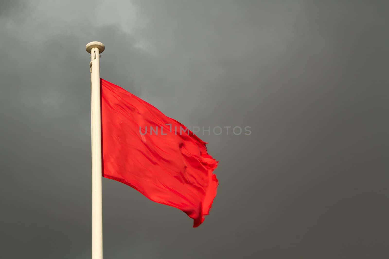 A white flag pole with a bright red flag against a grey cloudy sky.