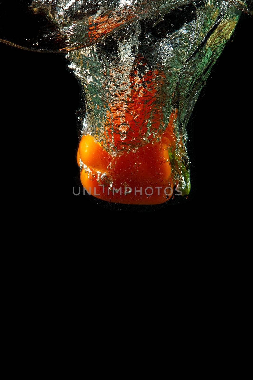 Colored orange paprika in water splashes on black background