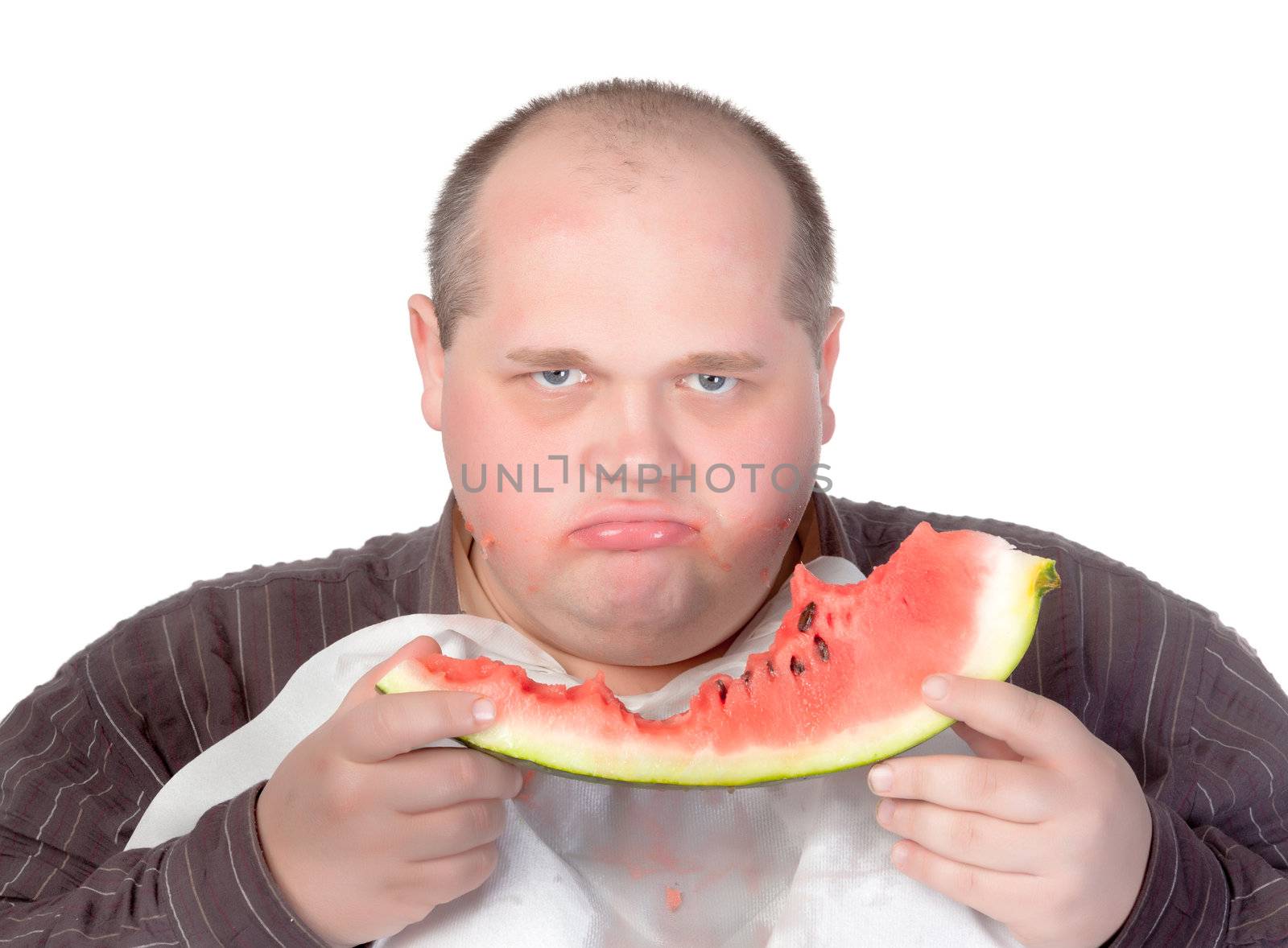 Obese man possessive of his food looking up from the slice of watermelon he is eating with a scowl and angry stare