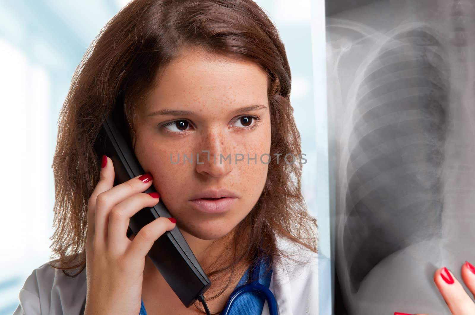 Young female doctor examining an x-ray while talking at the phone