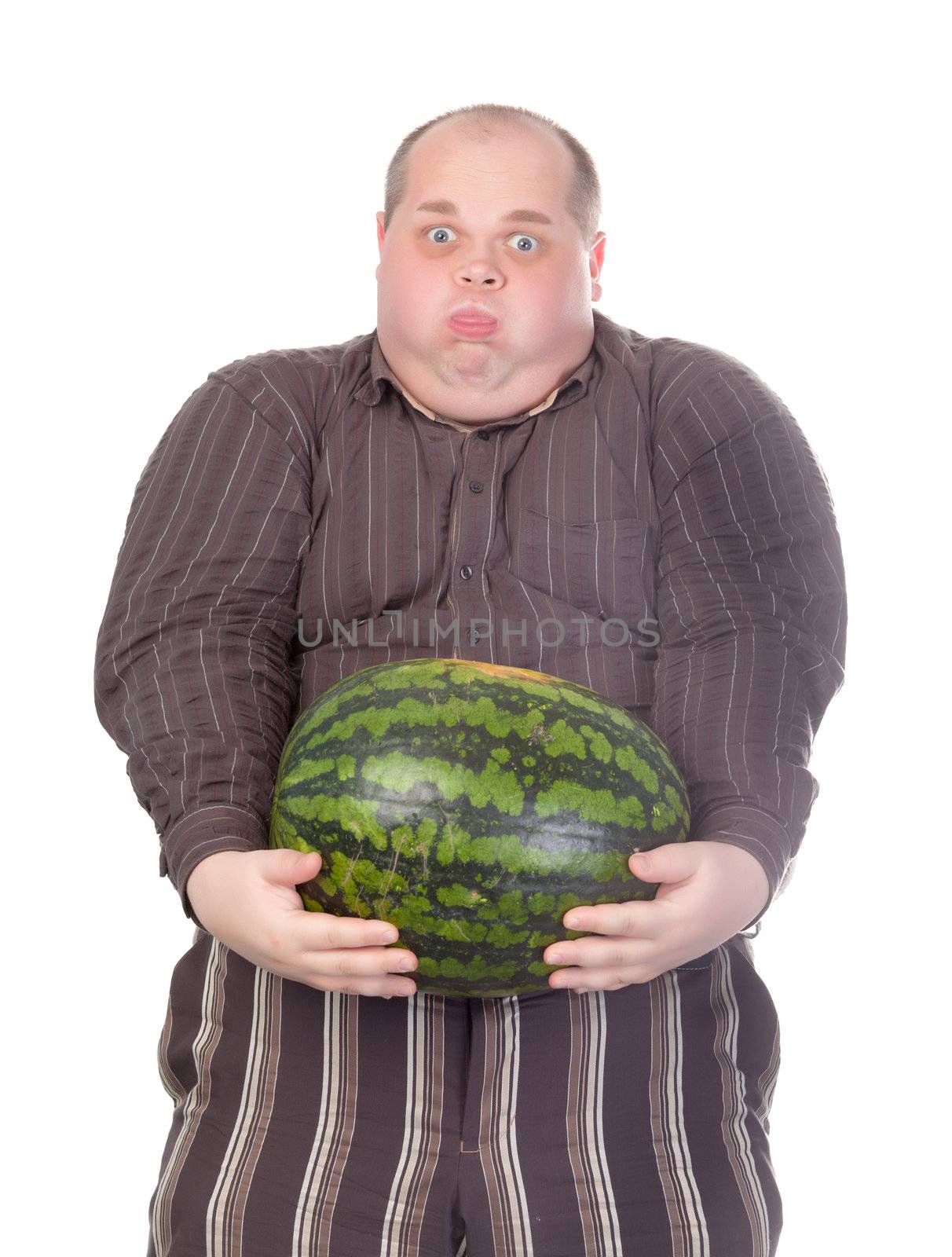 Humorous image of an unfit obese man struggling to hold the weight of a whole watermelon held at arms length in front of his huge protruding belly, isolated on white