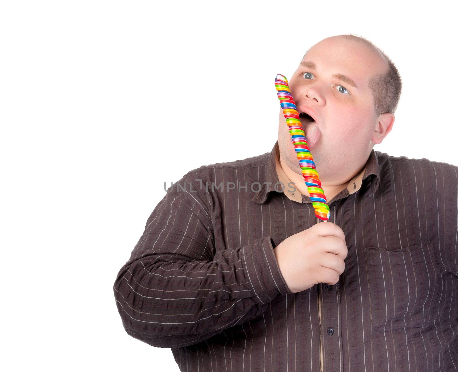 Fat obese man enjoying a a long colourful striped lollipop, standing licking it with a look of complete absorption totally oblivious to his surroundings