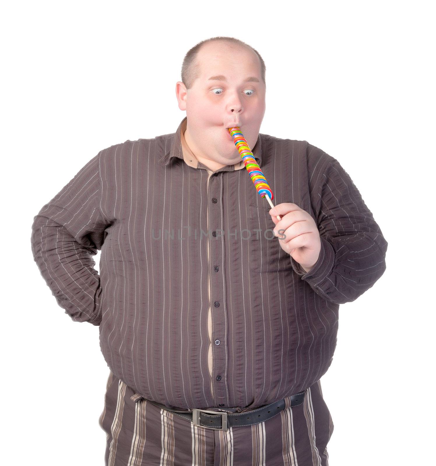 Fat obese man enjoying a a long colourful striped lollipop, standing licking it with a look of complete absorption totally oblivious to his surroundings