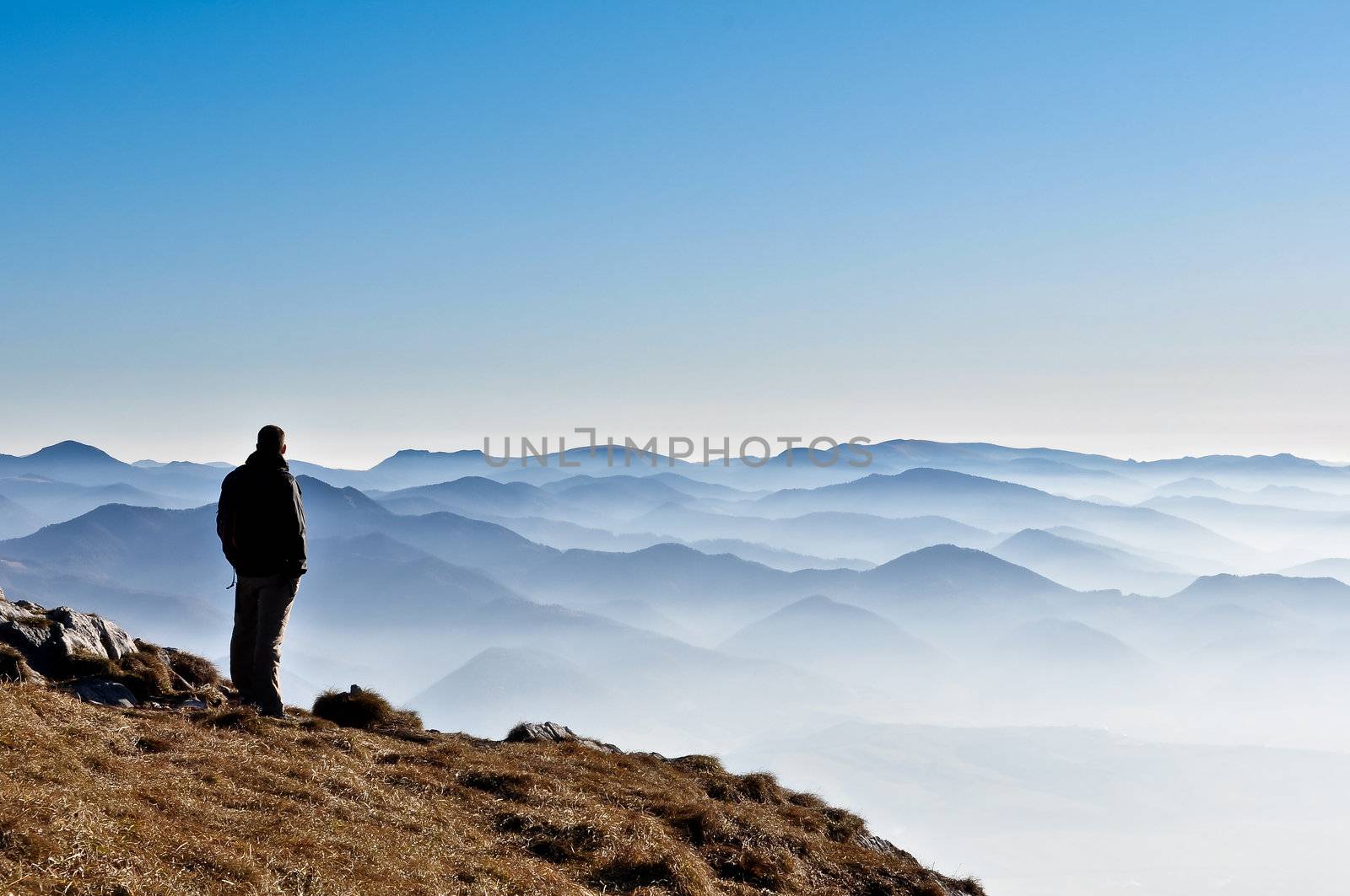 Misty mountain hills and man silhouette overlooking foggy mountains