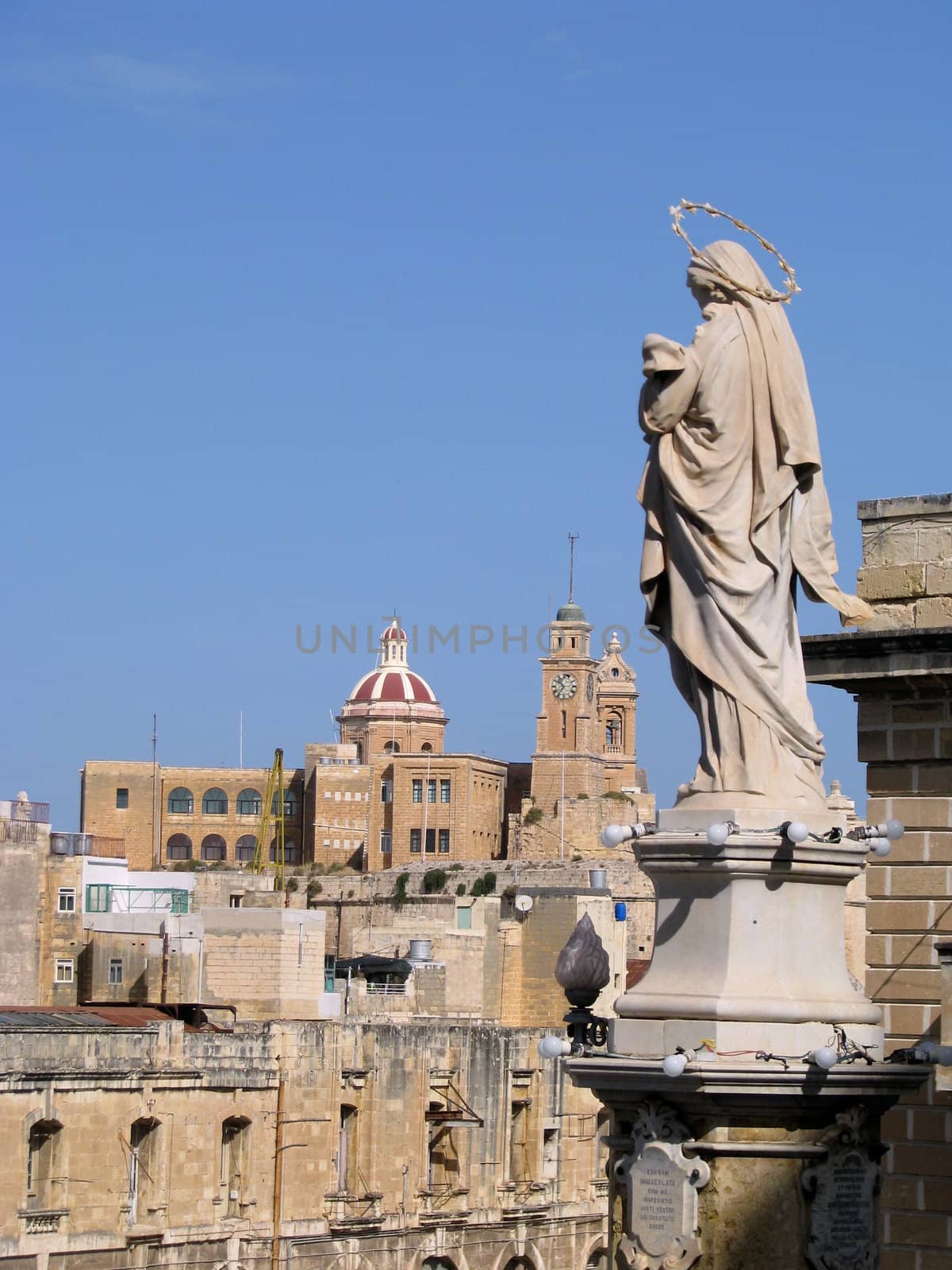 A marble statue of The Immaculate Conception in Cospicua - Malta with the church of Senglea in the background.