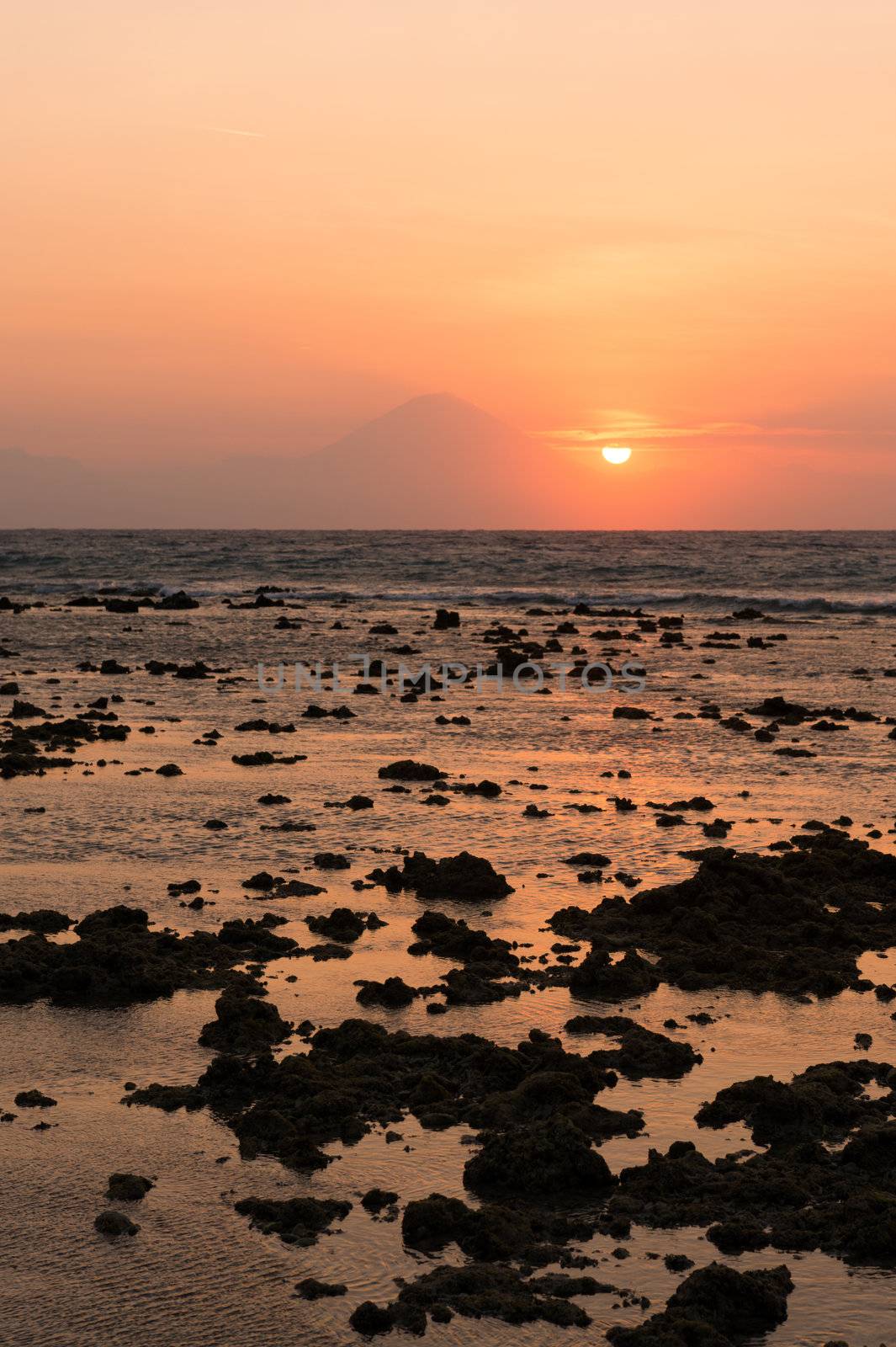 Warm tropical sunset over Agung volcano, the highest mountaint on Bali island, Indonesia with sea and stones on front