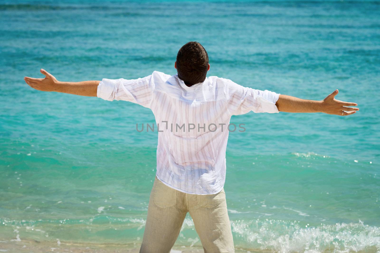 Rear view of happy man with outstretched arms on blue tropical sea