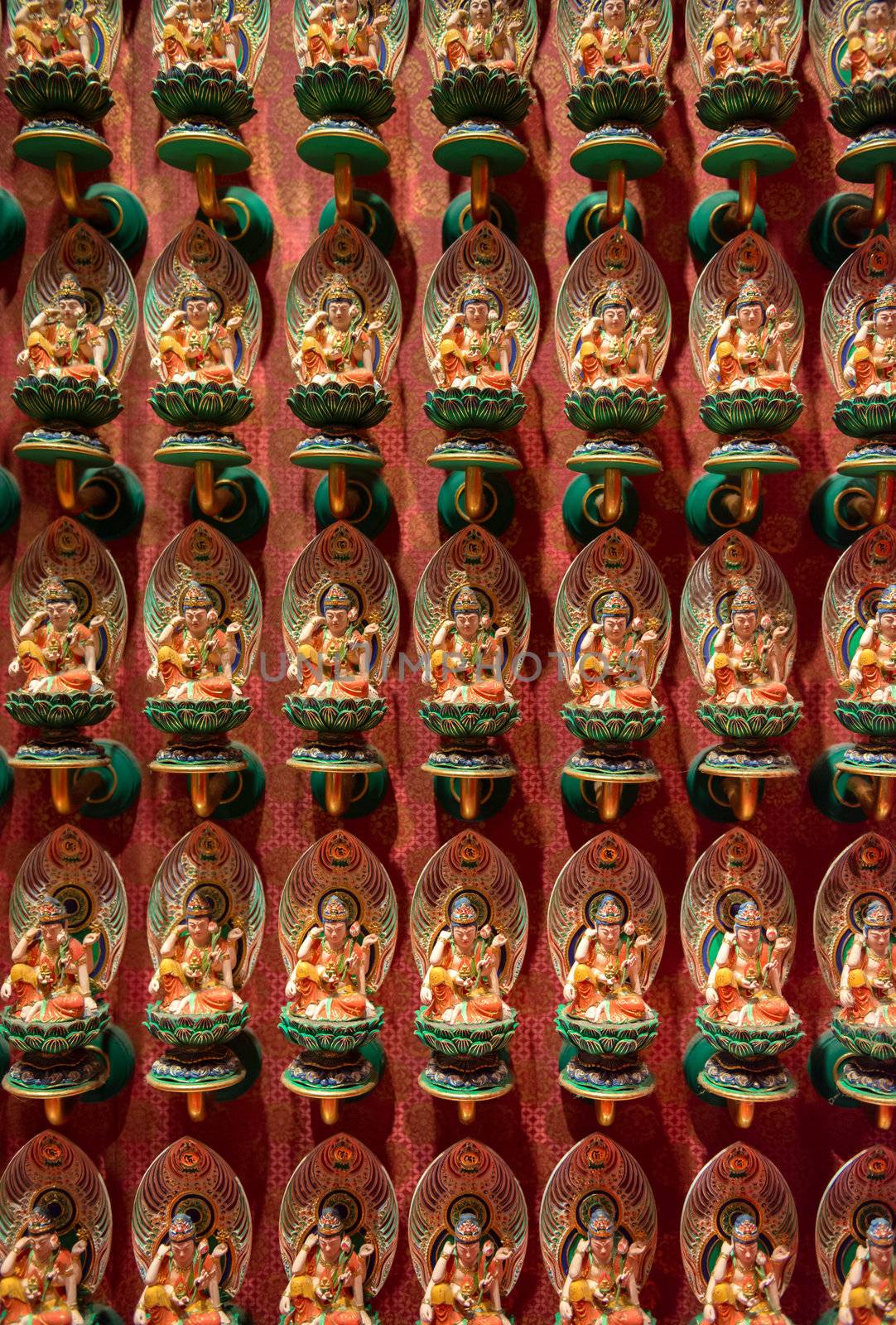Many small Buddhist statues on lotus flowers with red wall on background. Selective focus on front.